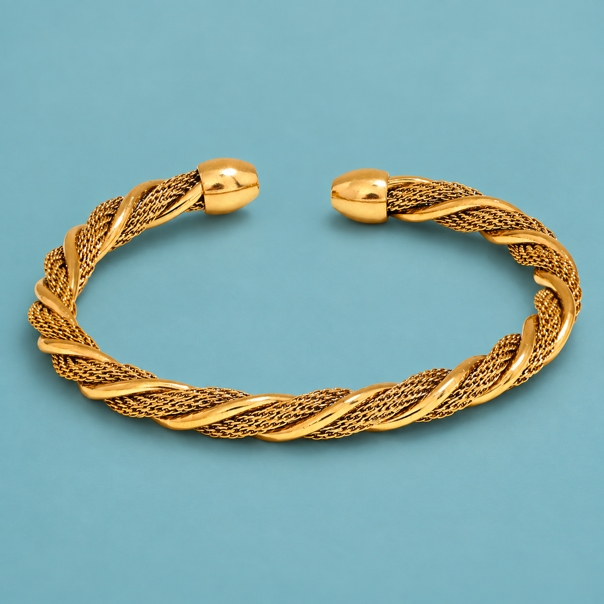 Gold-tone twisted mesh cuff on an aqua background