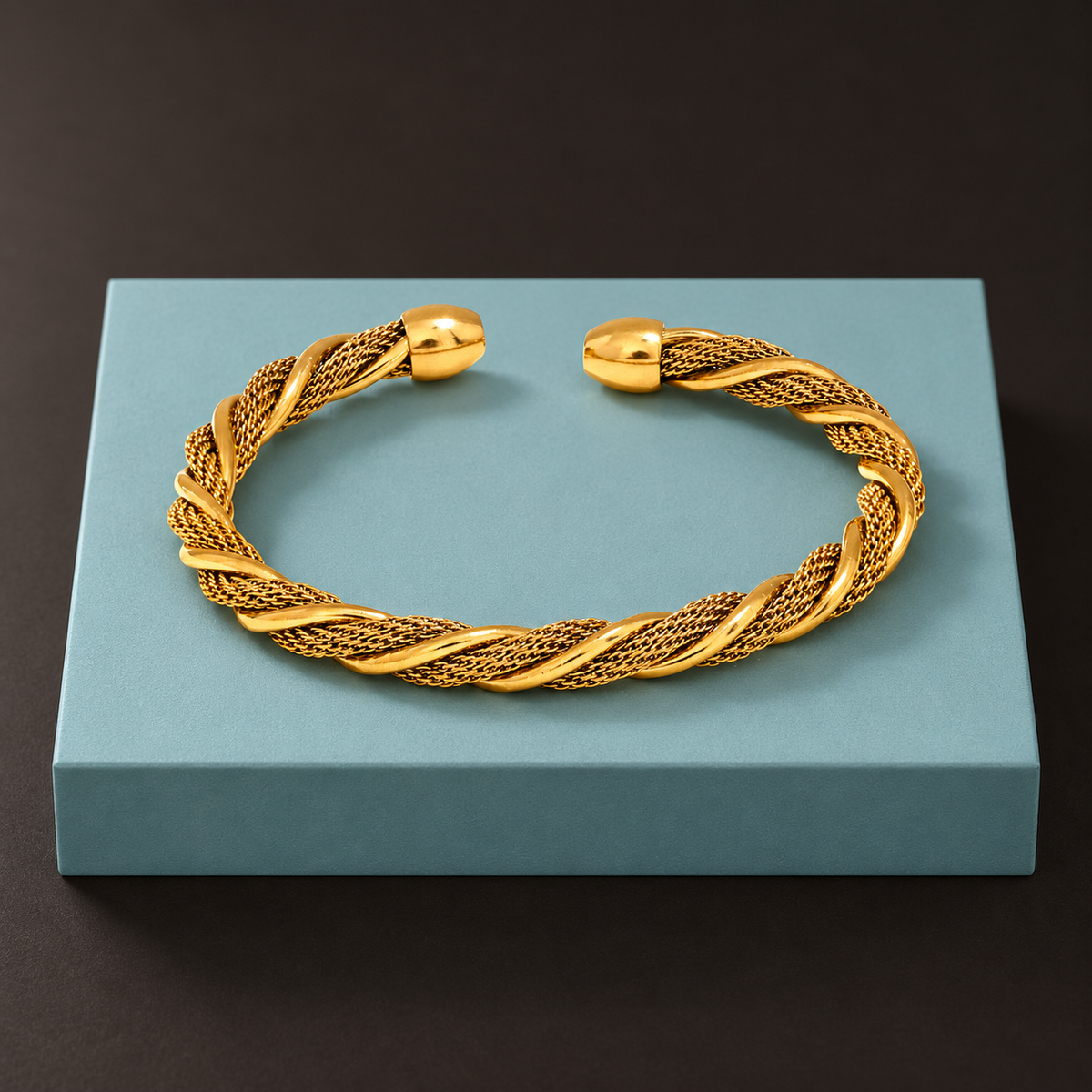 Gold-tone twisted mesh cuff displayed on an aqua block