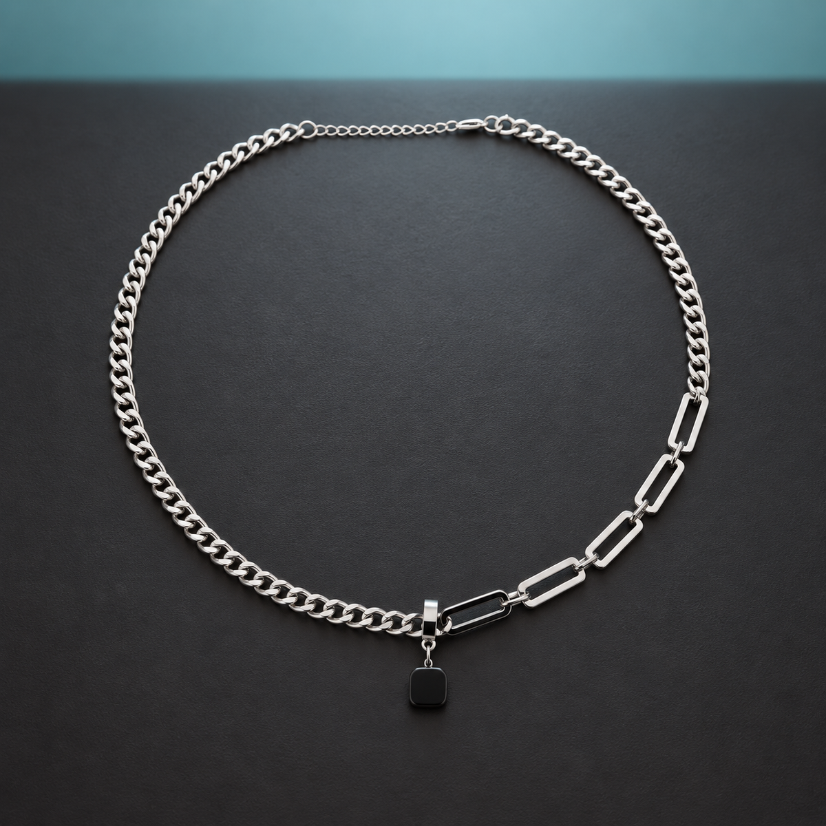 Black pendant and silver-tone link necklace on a charcoal surface