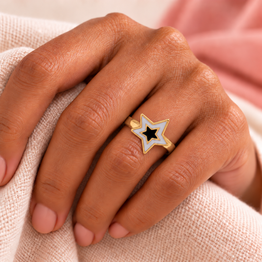 Pale and black nested-star ring styled on a hand with blush fabric