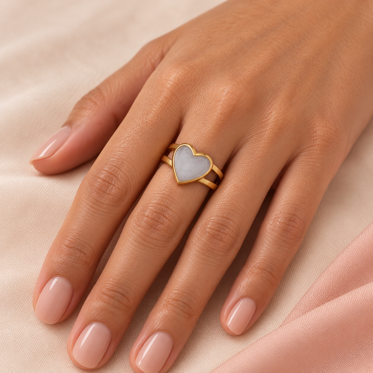 Pale heart ring shown on a hand resting on light fabric