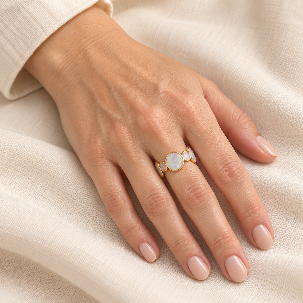 Pale circular-motif ring shown on a hand over light fabric
