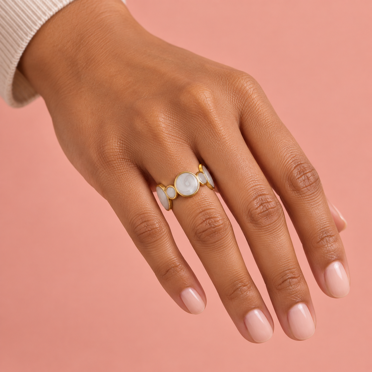 Gold-tone circular-motif ring shown on a hand against blush