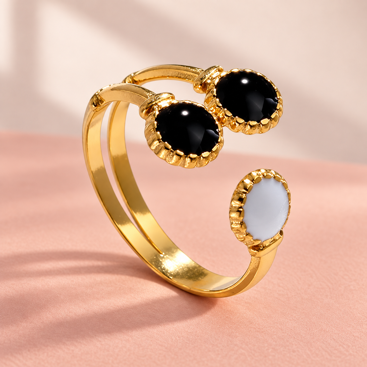 Gold-tone black and pale motif ring on a blush surface