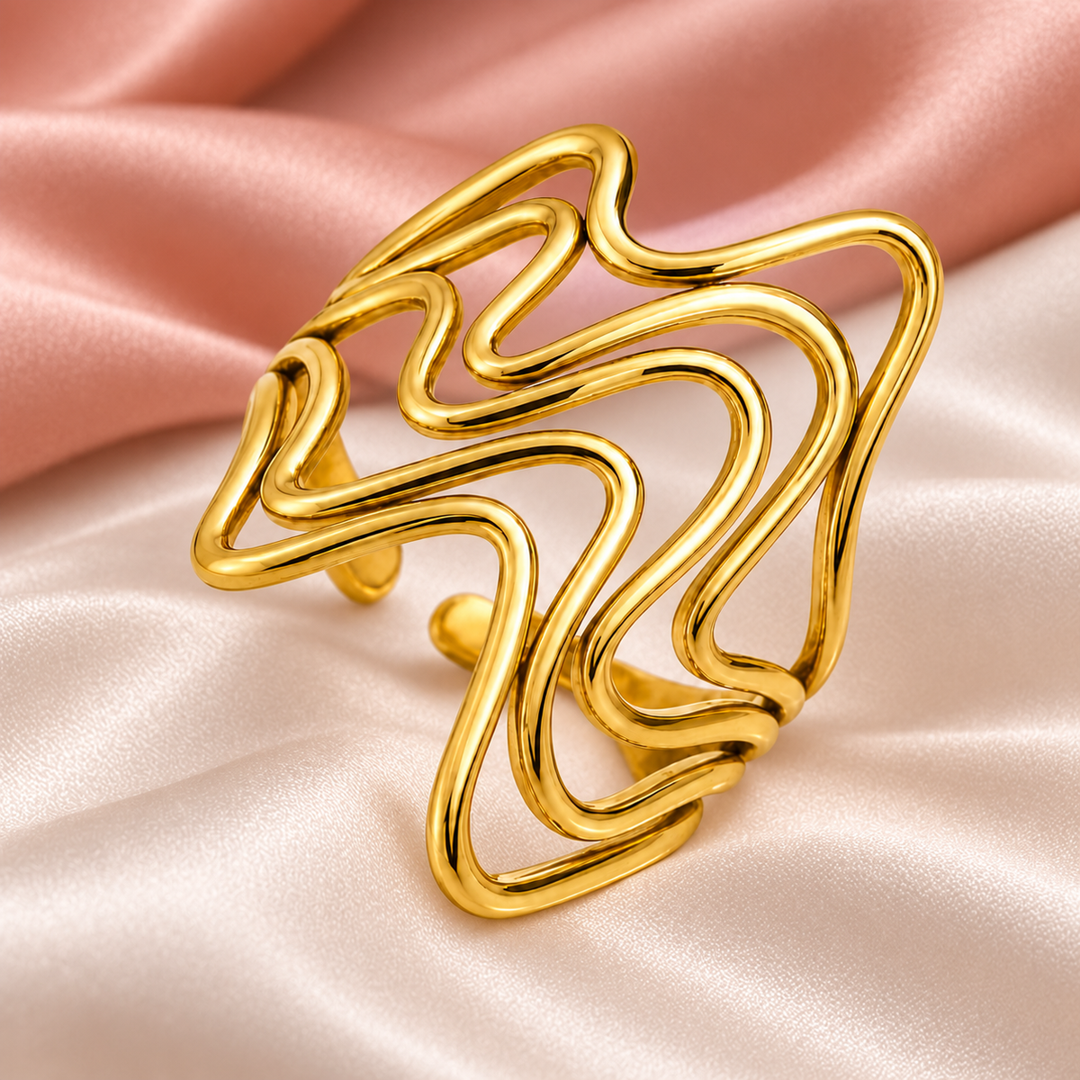 Gold-tone flowing wave ring, still-life view on fabric.