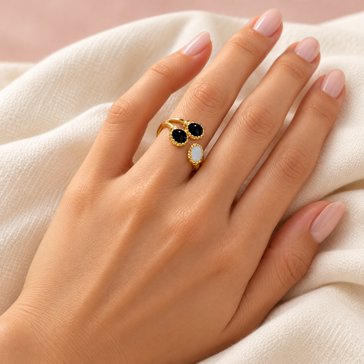 Gold-tone bypass ring with two black circles and one pale oval styled on a hand